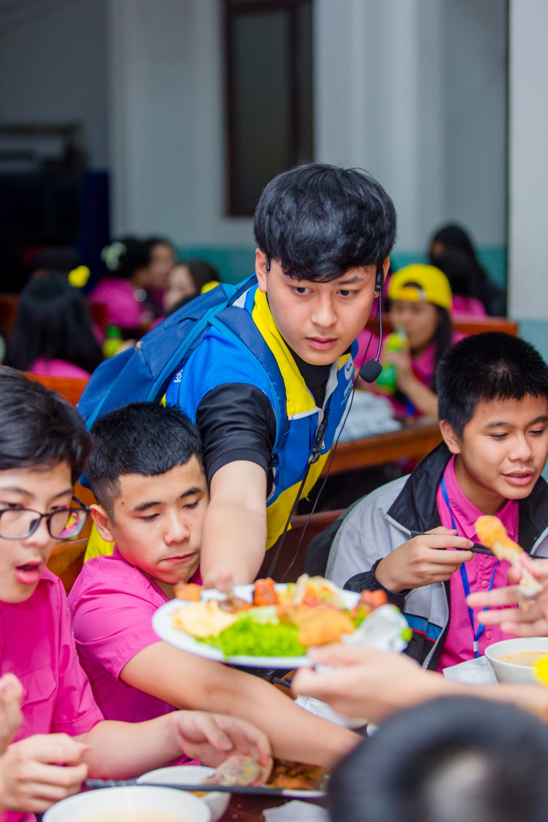 Hướng dẫn viên của trung tâm đang hướng dẫn và chăm sóc bữa trưa cho các em học sinh